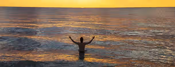 Embracing the Dawn of Leadership A person stands with arms raised in calm waters at sunrise, symbolizing an emerging leader embracing growth and new beginnings.