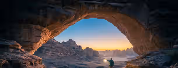 Illuminating Path of Emerging Leadership A lone figure illuminated by a lantern, stepping through a grand rock arch into a sunlit valley, symbolizing the dawn of new leadership.