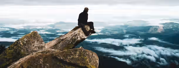 Summit of Self-Discovery: An Emerging Leader's Ascent A solitary figure sits on a mountain peak, overlooking vast, cloud-covered valleys, symbolizing the heights reached through self-improvement.