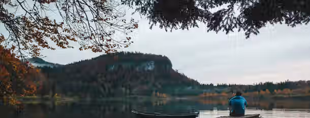 Reflecting on the Path to Leadership A contemplative figure sits by a tranquil lake, symbolizing the introspective journey of an emerging leader seeking self-improvement.