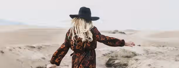 Journey Across the Sands of Self-Discovery A woman stands in an expansive desert, arms wide, symbolizing the journey of an emerging leader embracing self-improvement.