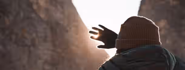 Reaching Toward the Light of Self-Discovery A lone figure reaches towards sunlight breaking through a mountain pass, symbolizing a leader finding their path to self-improvement.